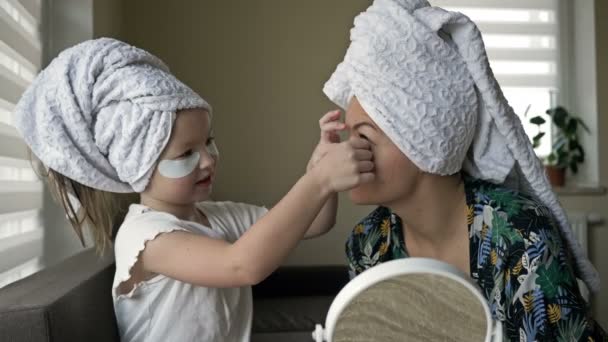 6-7 letá dívka pomáhá své matce aplikovat kosmetické náplasti pod očima. Ženy se starají o svou krásu. — Stock video