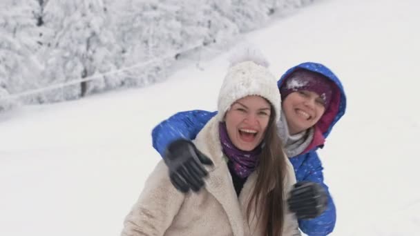 Dos mujeres jóvenes disfrutan de la nieve como niños. — Vídeos de Stock