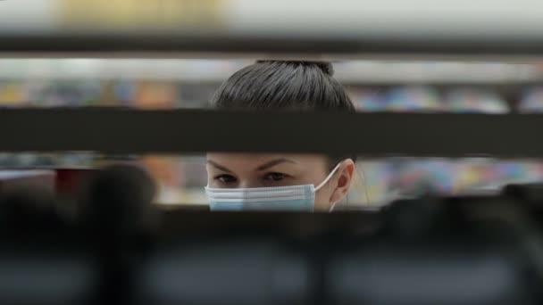 Jeune femme dans un masque de protection choisit quelque chose sur les étagères dans le magasin. Shopping pendant la pandémie de coronavirus. — Video