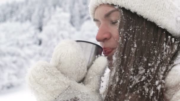 Retrato de uma bela jovem que bebe alguma bebida quente depois de uma luta de bolas de neve. — Vídeo de Stock