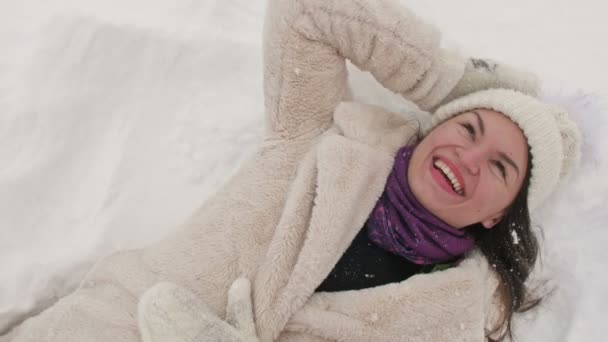 Mladá žena leží ve sněhu a vesele se směje. — Stock video