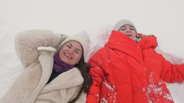 若い女性と10代の少女が雪の上に横たわっている。彼らは雪の中で喜ぶ。冬休み. — ストック動画