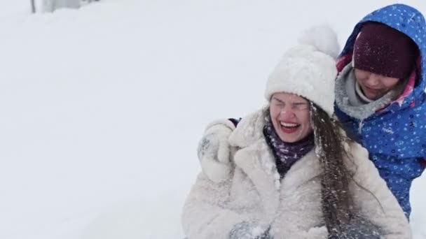 Dvě mladé veselé ženy sjely z kopce a spadly do sněhové závěje. Přítelkyně se dobře baví.. — Stock video