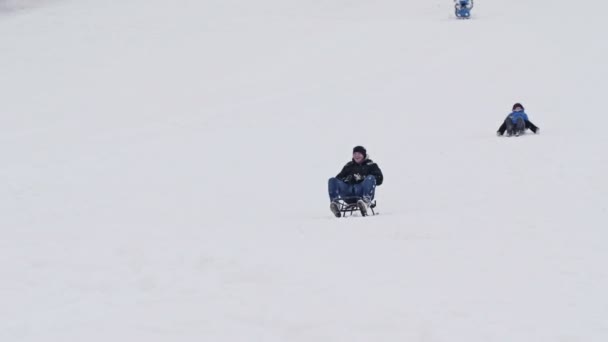 Anak muda tidur menuruni lereng bersalju. Kereta luncur berguling dan ia jatuh ke salju. Itu membuatnya bahagia.. — Stok Video