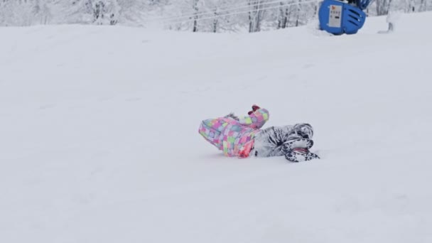 Radosna siedmiolatka podjeżdża i zjeżdża po śnieżnym stoku. Dziecko jest szczęśliwe.. — Wideo stockowe