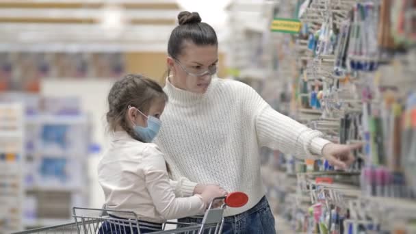Madre e bambino indossano maschere protettive scelgono articoli di cancelleria al supermercato. Shopping con i bambini durante l'epidemia di virus. — Video Stock
