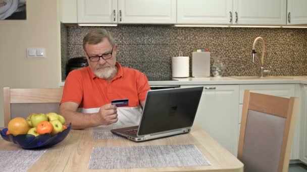 Idősebb férfi a laptopnál bankkártyával fizet az online vásárlásért. — Stock videók