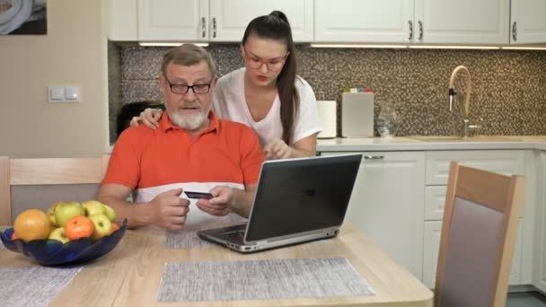 Schöne junge Frau erklärt ihrem älteren Vater, wie man online einkauft. — Stockvideo