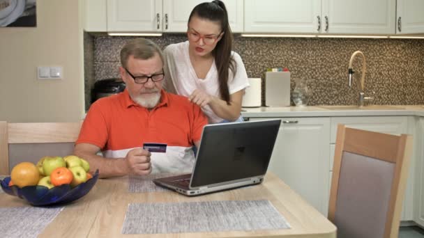 Jonge vrouw legt uit aan haar oudere vader hoe te winkelen en te betalen rekeningen van nutsbedrijven online. — Stockvideo