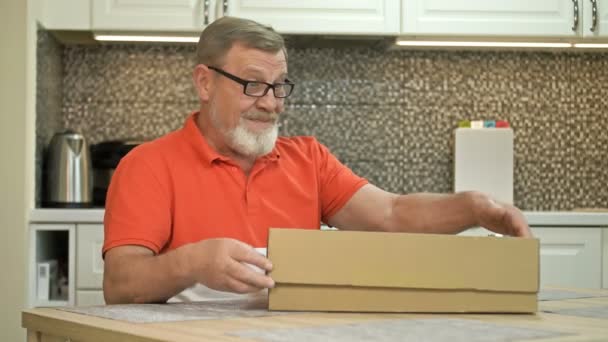 Glad äldre man packar upp ett paket. En nöjd regelbunden kund av kurirleveranstjänsten. Onlineshoppning. — Stockvideo