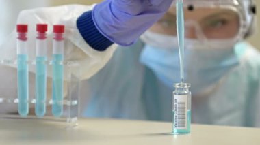 Koruyucu gözlüklü ve maskeli profesyonel kadın bilim adamı laboratuvarda reaktörlerle deney yapıyor. Koronavirüse karşı aşı üretimi.
