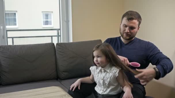 Opiekuńczy tata próbuje czesać swoje córki długimi włosami. — Wideo stockowe