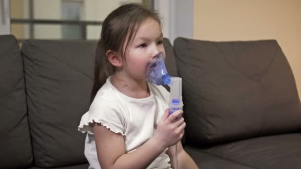 A kislány maszkkal az arcán lélegzik otthon. A gyermek szorgalmasan lélegzik.. — Stock videók
