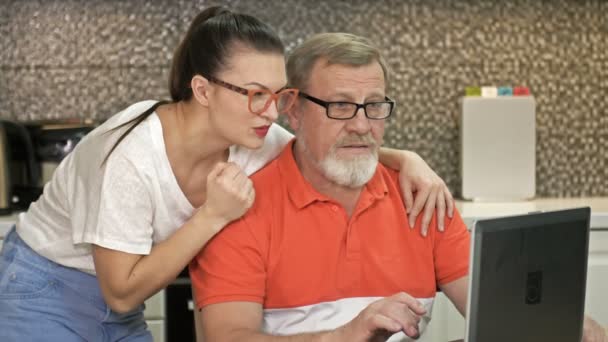 Schattige brunette en haar vader staren aandachtig naar het laptopscherm. Goed nieuws veroorzaakt een storm van positieve emoties.. — Stockvideo