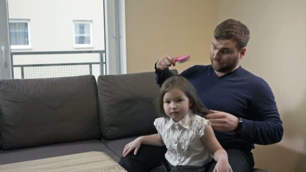 Młody mężczyzna próbuje czesać swoje córeczki długimi włosami. — Wideo stockowe