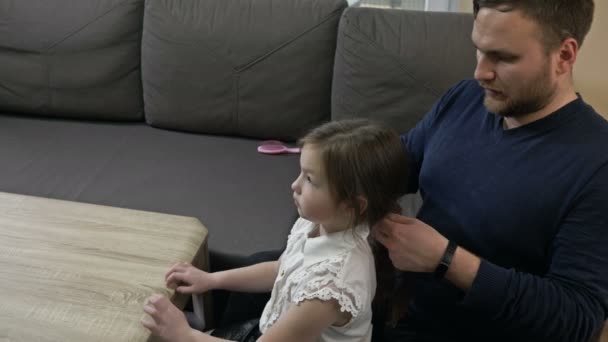 Middelbare man probeert zijn dochters vlechten te vlechten. Hij is er slecht in. Vaderdag. — Stockvideo
