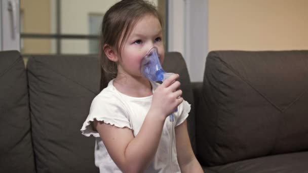 A kislány maszkkal az arcán lélegzik otthon. A gyermek szorgalmasan lélegzik.. — Stock videók