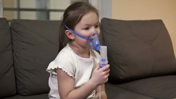 La niña pequeña inhala con una máscara en la cara en casa. El niño respira diligentemente. — Vídeos de Stock