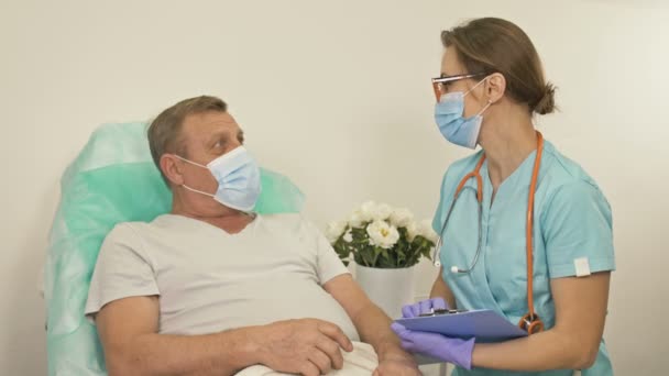 O médico fala com um paciente idoso numa enfermaria. Mulher alegra o paciente. — Vídeo de Stock