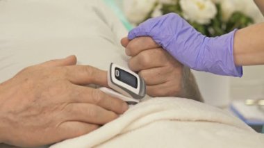 Kadın doktorlar, hastanenin acil servisinde yatakta yatan ve ciddi semptomları olan yaşlı bir hastanın elini tutuyor..