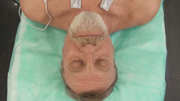 En äldre man som ligger på en sjukhussäng vaknar upp efter operationen. — Stockvideo