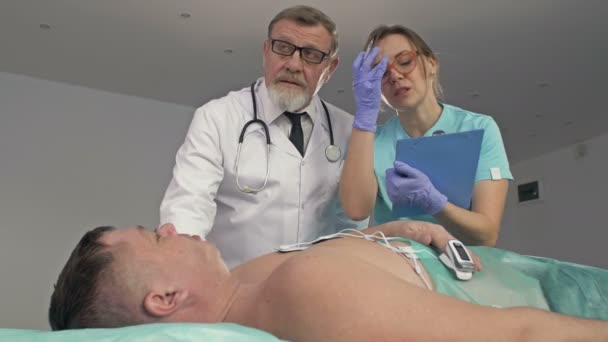 Médicos examinando a un paciente masculino críticamente enfermo en la sala de emergencias. — Vídeo de stock