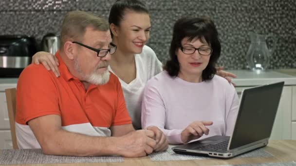 Belle jeune femme explique à ses parents âgés comment faire des achats et divers paiements en ligne. Compétences nécessaires dans des conditions modernes. — Video