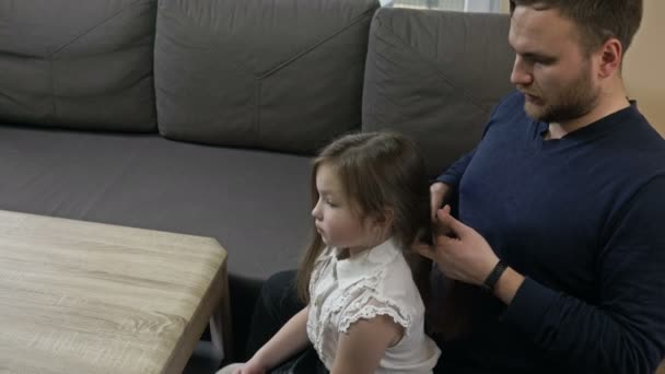 Vårdande pappa klumpigt flätar en liten dotter flätor. — Stockvideo