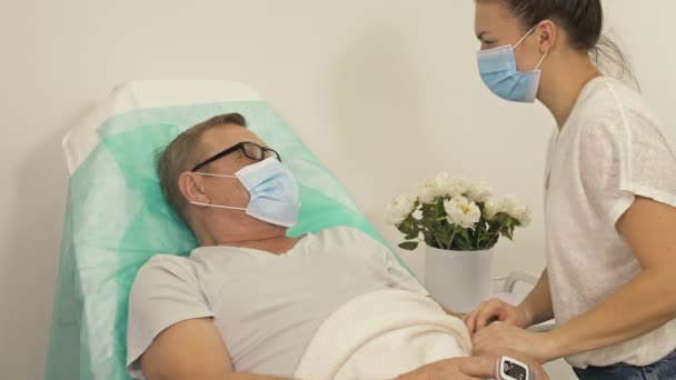 Доросла дочка відвідала батька, який знаходиться в лікарні. Обидва носять медичні маски, необхідну під час педемії Ковід-19.. — стокове відео