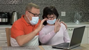 Tıbbi maskeli neşeli evli çift internet üzerinden biriyle iletişim kuruyor. Modern teknolojiler. Koronavirüs salgını sırasında iletişim kurma yeteneği.