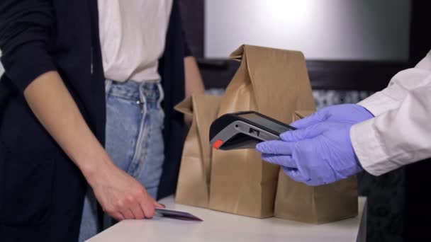 Der Käufer bezahlt den Einkauf mit einer Plastikkarte. Der Verkäufer in Schutzhandschuhen. Handel inmitten der Coronavirus-Pandemie. — Stockvideo