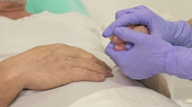 Yakın plan. Doktorlar yaşlı bir hastanın elini tutuyorlar. Destek jesti.