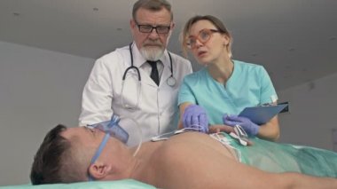 Acil serviste durumu kritik olan bir erkek hastayı muayene eden yaşlı bir doktor ve hemşire..