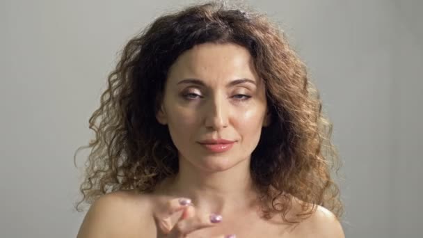 Hermosa mujer madura aplica crema a la piel de su cara con movimientos ligeros. Cuidado corporal. Tratamientos cosméticos y anti-envejecimiento. — Vídeo de stock