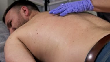 Balmumu olan erkeklerde sırtında epilasyon. Orta yaşlı bir adam güzellik salonunda epilasyon yaparken acı çekiyor..