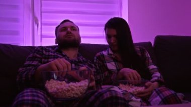 Evli çift televizyon izliyor ve patlamış mısır yiyor. Covid-19 salgını sırasında ev karantinası.