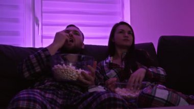 Evli çift televizyon izliyor ve patlamış mısır yiyor. Çiftler eğleniyor. Covid-19 salgını sırasında ev karantinası.