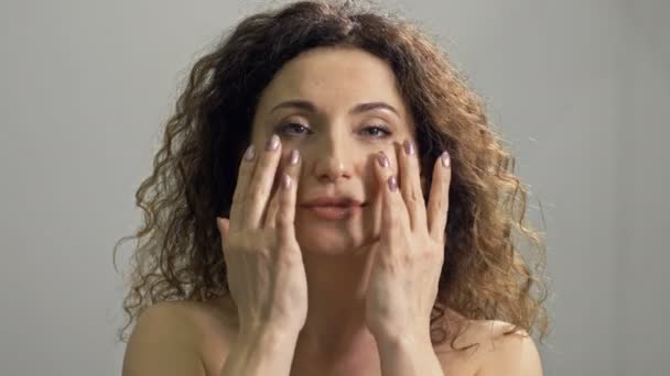 Hermosa mujer de mediana edad masajea su cara con movimientos ligeros. Cuidado diario de la piel. — Vídeos de Stock