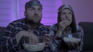 Evli çift televizyon izliyor ve patlamış mısır yiyor. Covid-19 salgını sırasında ev karantinası.