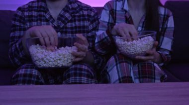 Pijamalı evli bir çift televizyonun önünde oturmuş patlamış mısır yiyor..