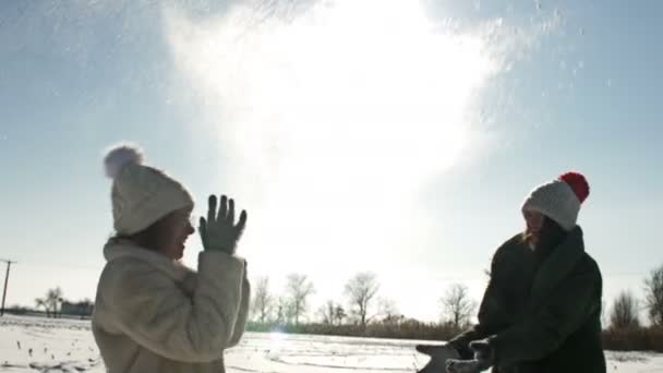 Dua gadis memercikkan salju satu sama lain. Winter walk, sunny day. — Stok Video