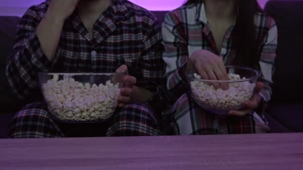 Супружеская пара в пижаме сидит перед телевизором и ест попкорн. Домашний карантин во время пандемии Ковида-19. — стоковое видео