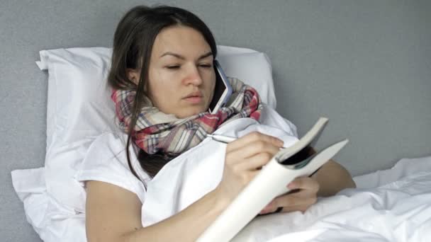 Больная молодая женщина лежит в постели с симптомами гриппа или коронавируса. Несмотря на это, она работает или учится удаленно. — стоковое видео