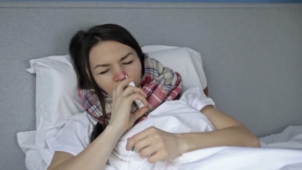 Giovane donna malata si trova a letto con influenza o sintomi di raffreddore o coronavirus. Donna spruzza medicina nel naso. — Video Stock