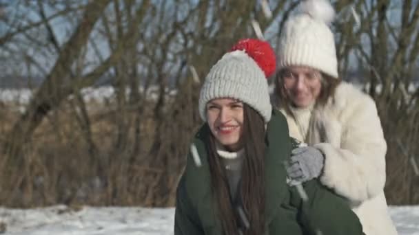 Mama i dorosła córka lub dwie siostry bawią się podczas zimowego spaceru i ktoś rzuca w nie śniegiem. — Wideo stockowe