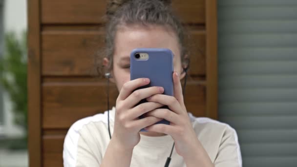 Έφηβη κοπέλα που κρατάει το τηλέφωνο παθιασμένη με τις εφαρμογές κοινωνικής δικτύωσης smartphone κάθεται μόνη της στο σπίτι. Τεχνολογία εθισμένος έφηβος παίζει κινητά παιχνίδια, γραπτών μηνυμάτων, βλέποντας βίντεο σχετικά με τη σύγχρονη τεχνολογία gadget. — Αρχείο Βίντεο