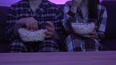 Pijamalı evli bir çift televizyonun önünde oturmuş patlamış mısır yiyor..