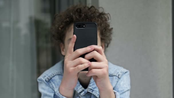 Boy gamer, jogando entusiasticamente um jogo em um telefone celular. Dependência moderna. — Vídeo de Stock