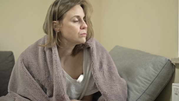 年轻妇女坐在被子里，用毯子测量温度。她有流感、感冒或大头牛的症状. — 图库视频影像