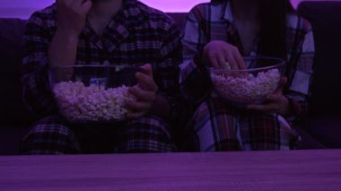 Pijamalı evli bir çift televizyonun önünde oturmuş patlamış mısır yiyor. Covid-19 salgını sırasında ev karantinası.